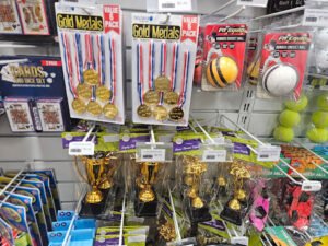 retail selection of sports awards and equipment, including medals, trophies, and cricket balls.